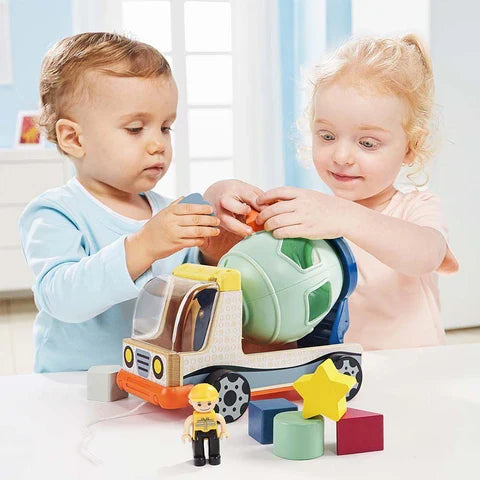 Two children play with a wooden cement mixer truck featuring a green shape-sorter drum and colorful geometric blocks.