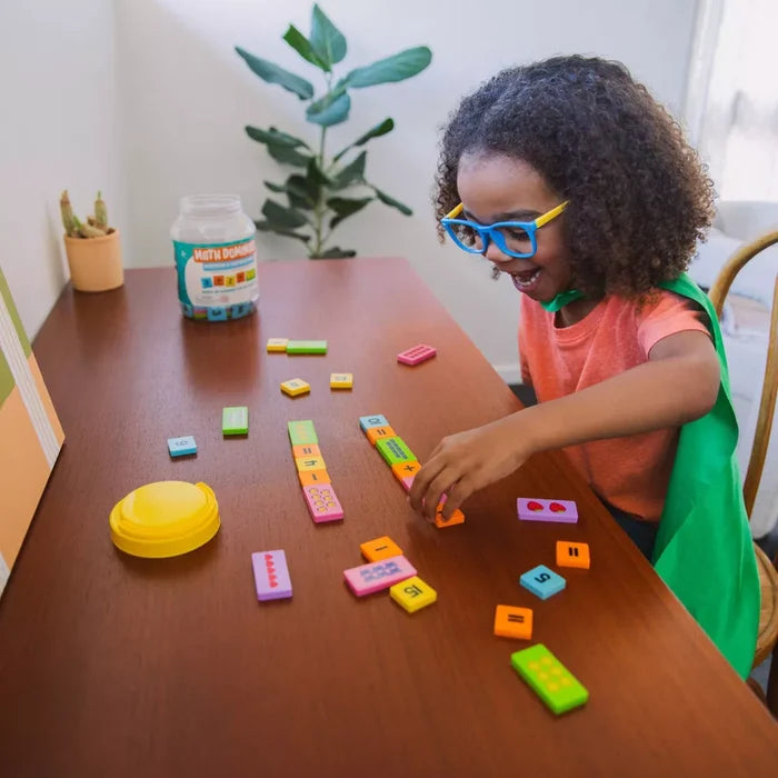 A child plays with colorful rectangular dominoes showing numbers and math equations on a wooden table.