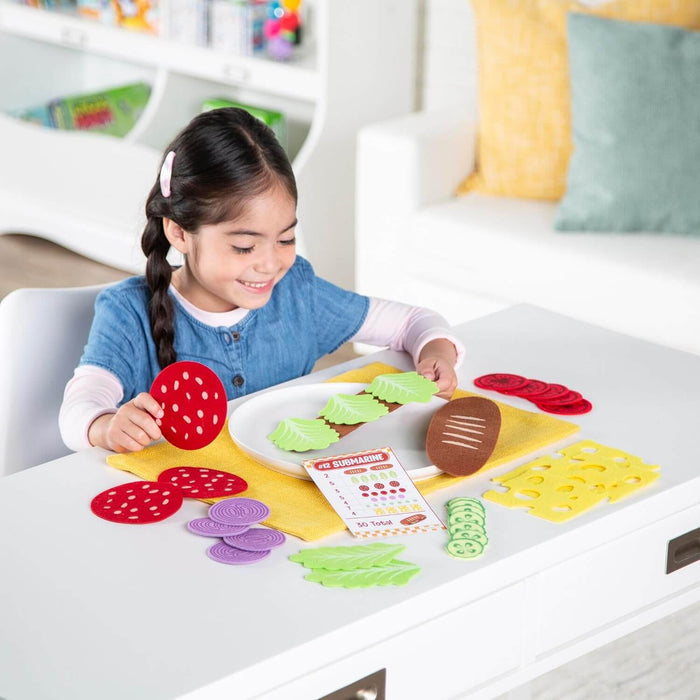 Child builds a felt sandwich with green lettuce, yellow cheese, and red salami using a numbered order card.