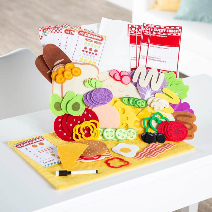 Felt sandwich set with colorful toppings, numbered menu cards, and guest checks on a yellow mat with a marker.