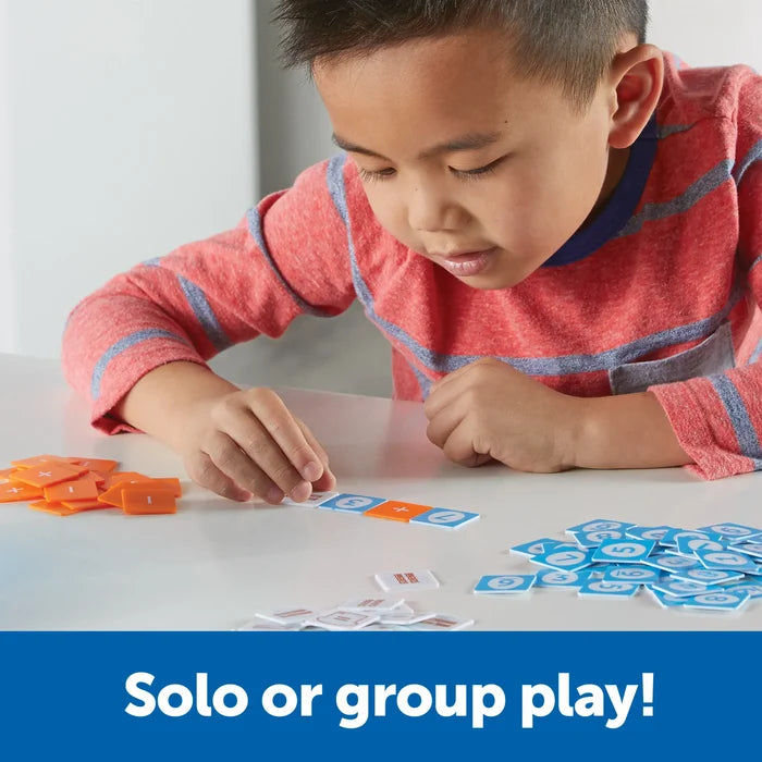 A child arranges blue, orange, and white tiles with numbers and math symbols to form an equation on a table.