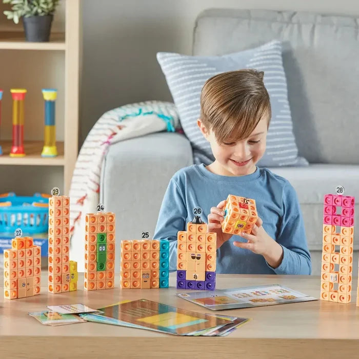 A boy building Numberblocks characters with colorful snap-together cubes and activity cards on a wooden table.