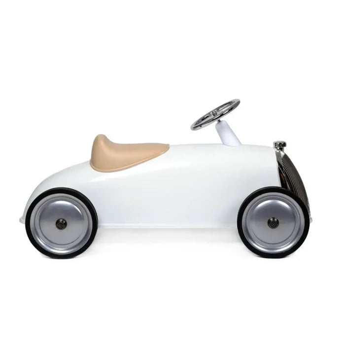Side profile of a white vintage-style ride-on car with a tan seat, chrome steering wheel, and silver wheels.