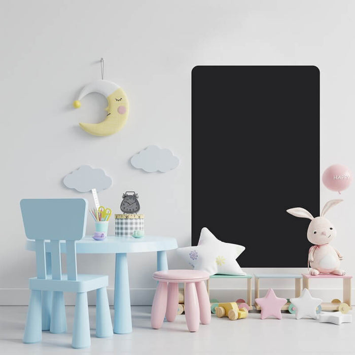 Black rectangular chalkboard with rounded corners mounted on a white wall in a playroom with light blue and pink furniture.