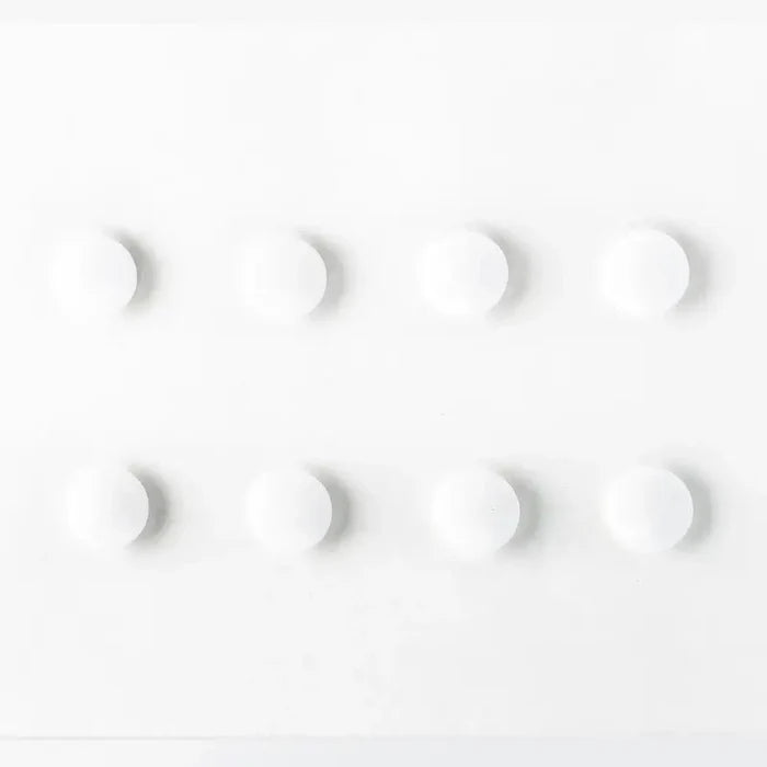 Eight white circular magnets in two rows of four on a plain white rectangular surface with soft shadows.