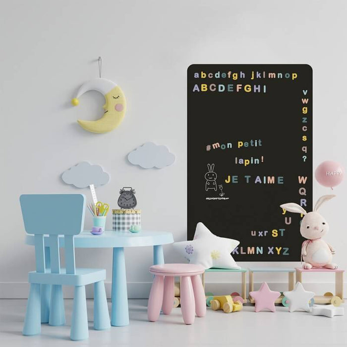 Black rectangular magnetic chalkboard on a playroom wall featuring colorful letters and white chalk drawings.