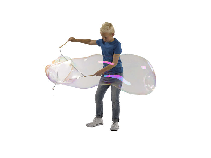 Boy in blue shirt using long sticks to create a massive, iridescent soap bubble against a white background.
