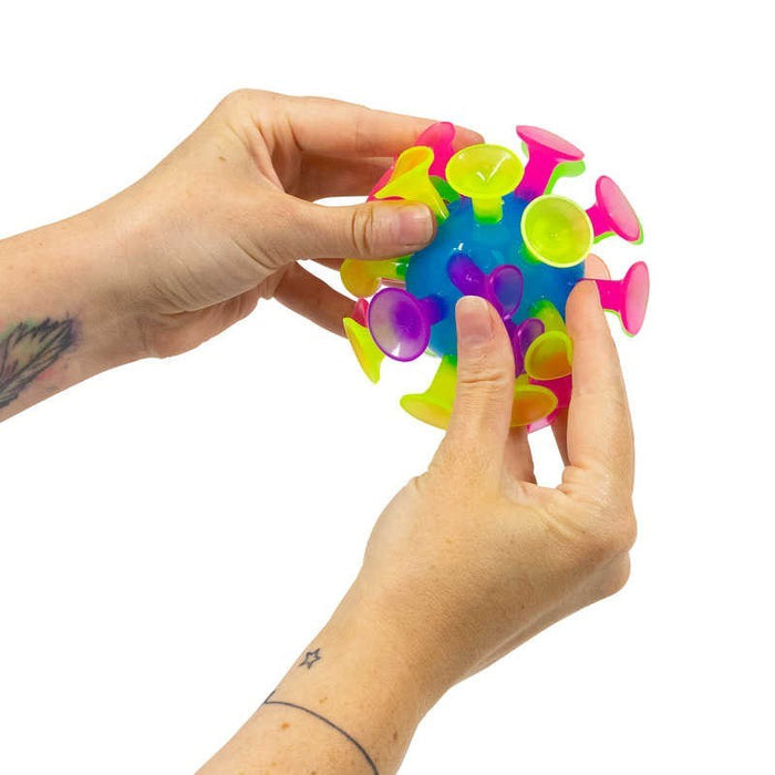 Hands holding a blue translucent ball covered in bright pink, yellow, and green suction cups.