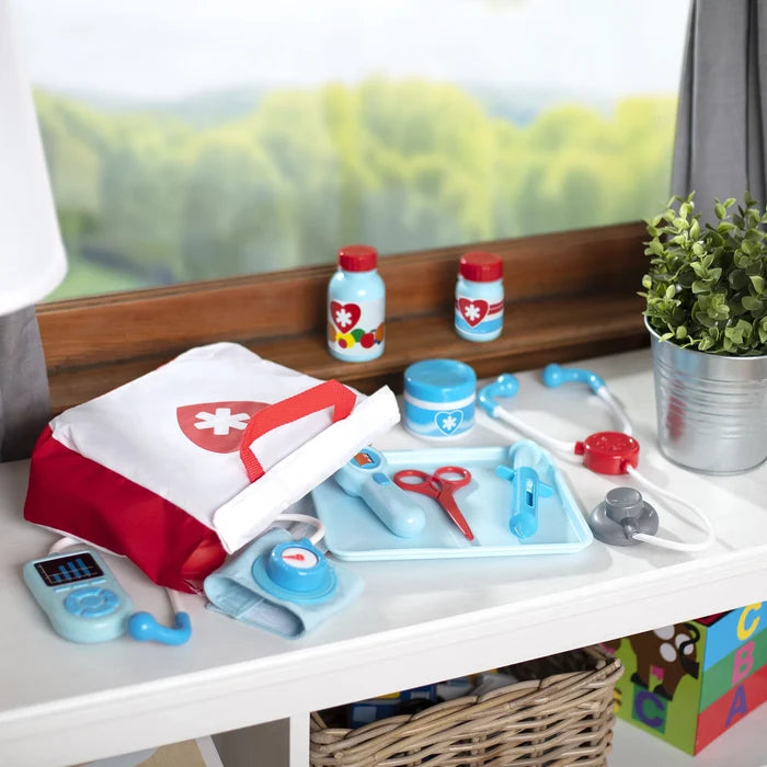 Red and white doctor bag with light blue medical toys, bottles, and a stethoscope displayed on a white surface.