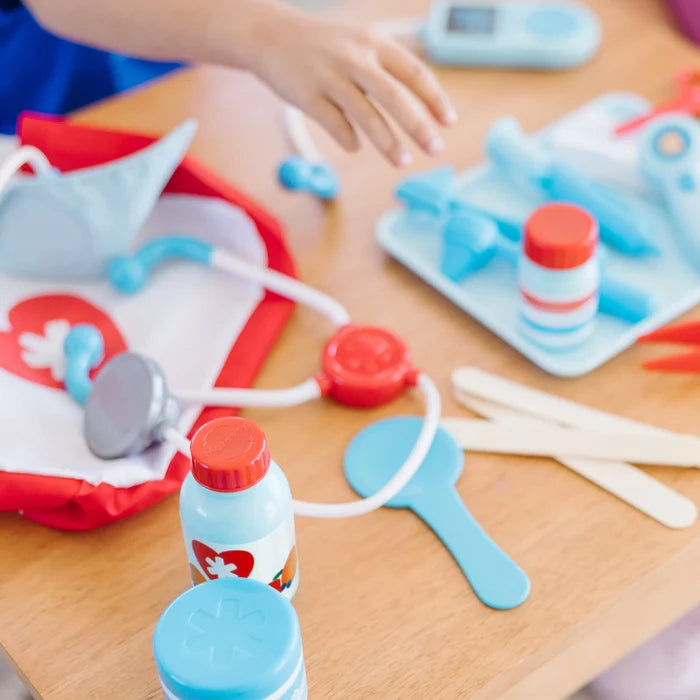 Child’s hand reaching for light blue and red toy medical tools including a stethoscope, bottles, and tongue depressors.
