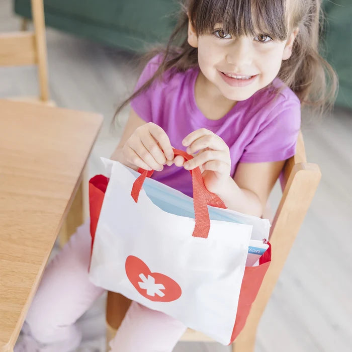 Young girl holding a white medical tote bag with red handles and a red heart with a cross icon.