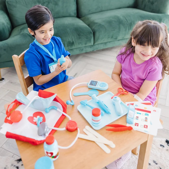 Two children play with a toy doctor kit featuring blue plastic medical tools, a stethoscope, and a red medical bag.