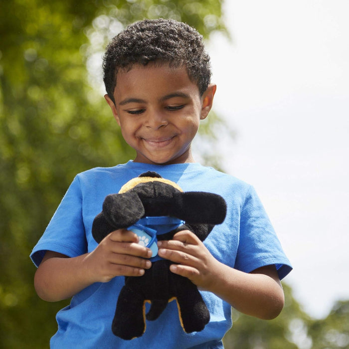 Young boy smiles holding a small black plush dog with a blue collar and paw print tag.