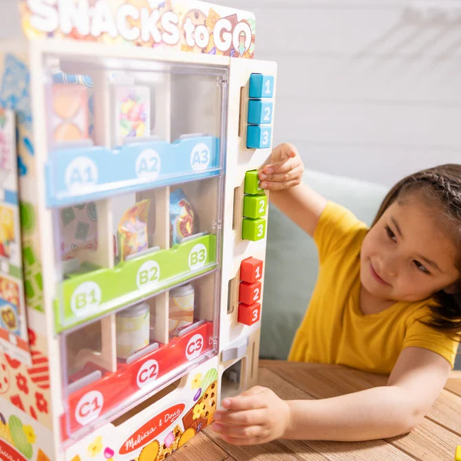 Child playing with a wooden snack vending machine toy featuring colorful push buttons and pretend snacks.