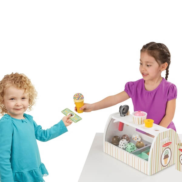 Two girls play with a wooden ice cream shop toy featuring colorful scoops, cones, and play money.
