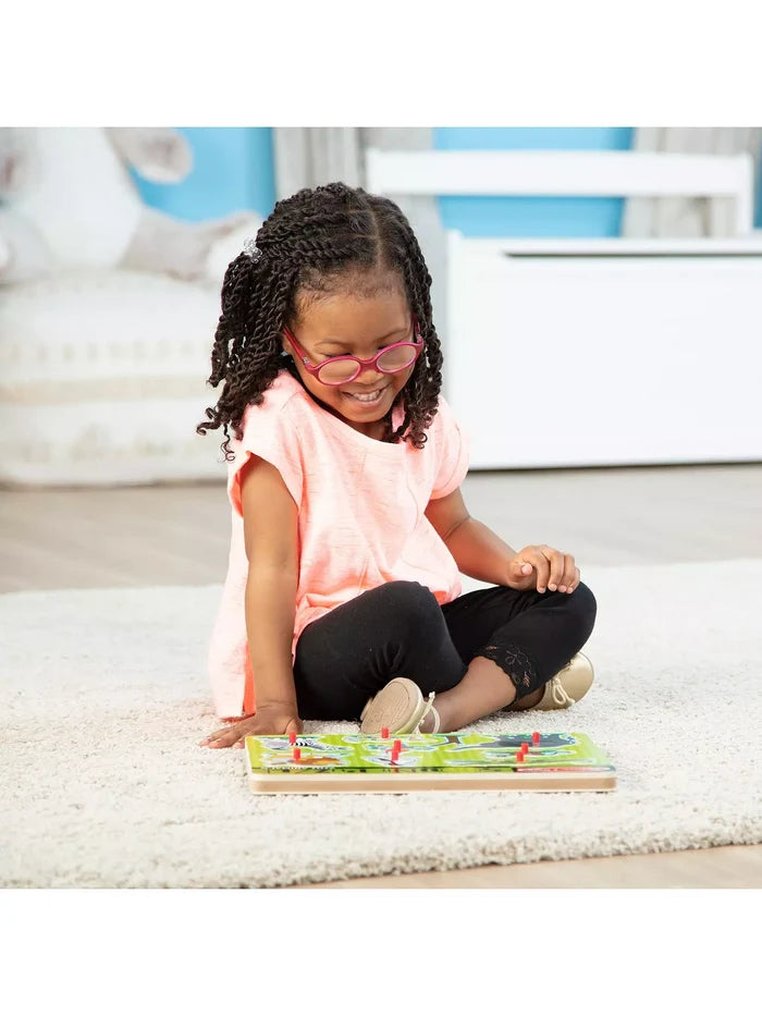 Young girl smiling while playing with a wooden zoo animal peg puzzle on a white rug.