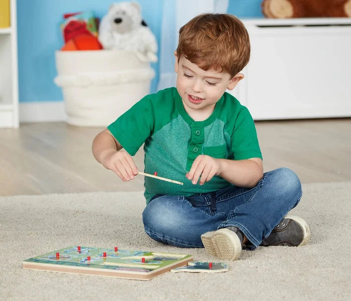A young boy plays with a wooden zoo animal puzzle featuring red pegs on a light-colored rug.
