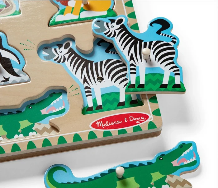 Wooden peg puzzle with zoo animal pieces lifted to reveal matching illustrations of a zebra and crocodile.