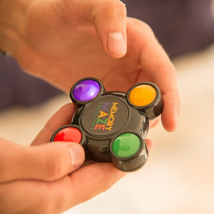 Hands holding a circular black electronic game featuring purple, yellow, red, and green light-up buttons.