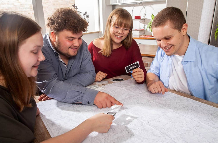 Four people gathered around a table, pointing at a large black and white city map and holding small clue cards.