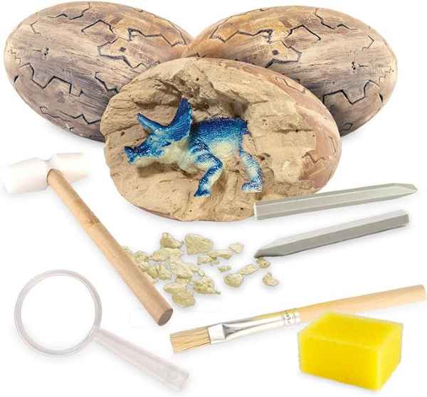 Excavation kit with three textured eggs, a blue dinosaur toy, wooden hammer, chisels, brush, and magnifying glass.