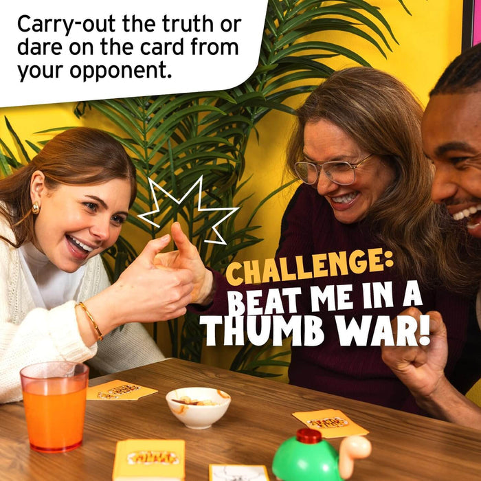 Three friends laughing while thumb wrestling over a wooden table with game cards and a small green turtle figure.