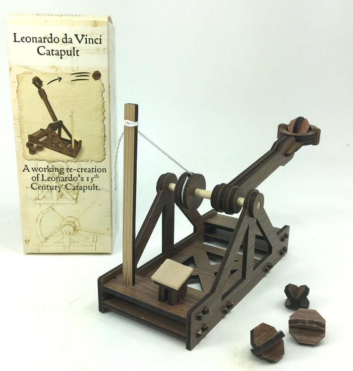 Dark brown wooden catapult model with white string and three projectiles, displayed next to its illustrated box.