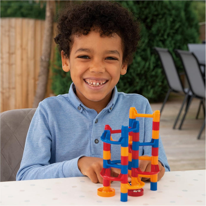 Smiling boy with a colorful red, yellow, and blue plastic marble run featuring towers and winding chutes.