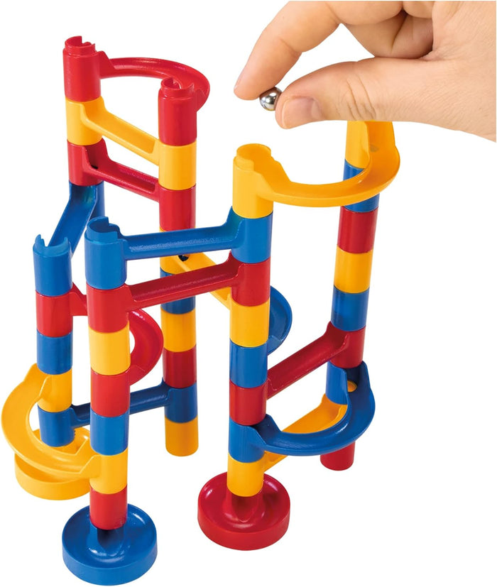 Hand dropping a silver marble into a colorful red, yellow, and blue plastic toy with interlocking towers and tracks.