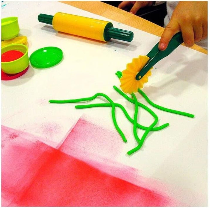 Child's hand using a yellow and green dough cutter and rolling pin with green dough and colorful containers.