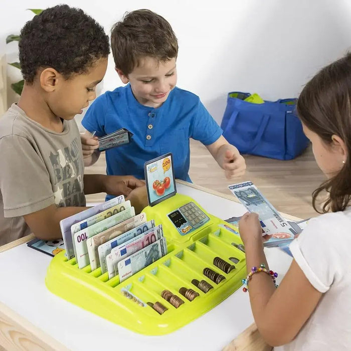 Three children playing with a bright green toy tray filled with play euro banknotes and stacks of coins.