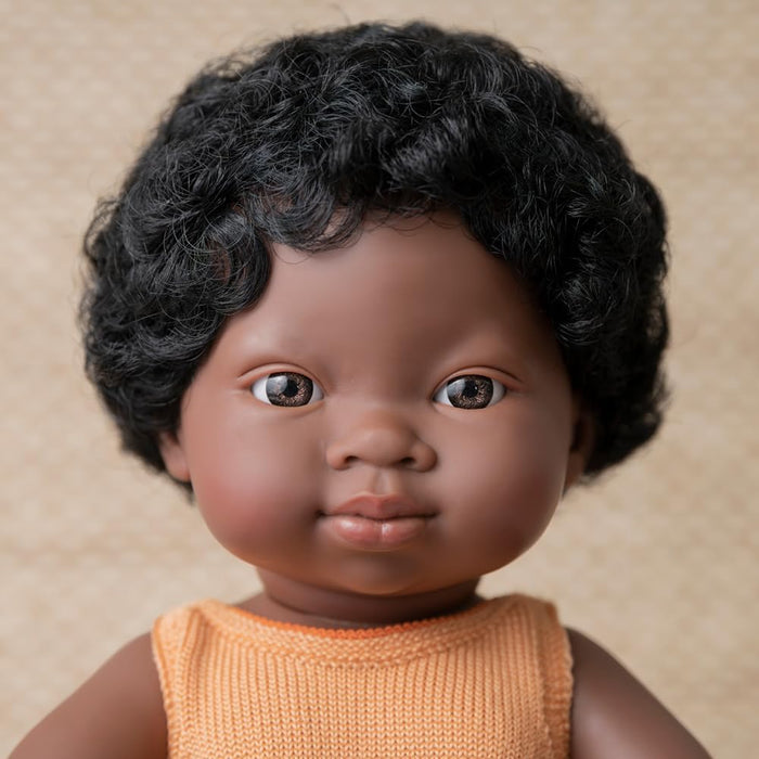 Close-up of a dark-skinned doll with curly black hair and brown eyes wearing an orange knitted tank top.