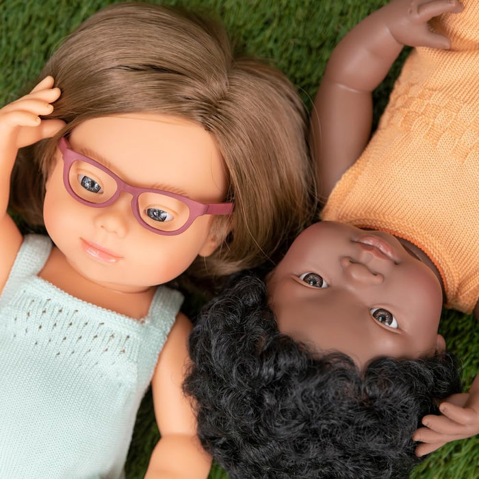 Dark-skinned doll with curly black hair and orange knit top lying on green grass next to another doll.