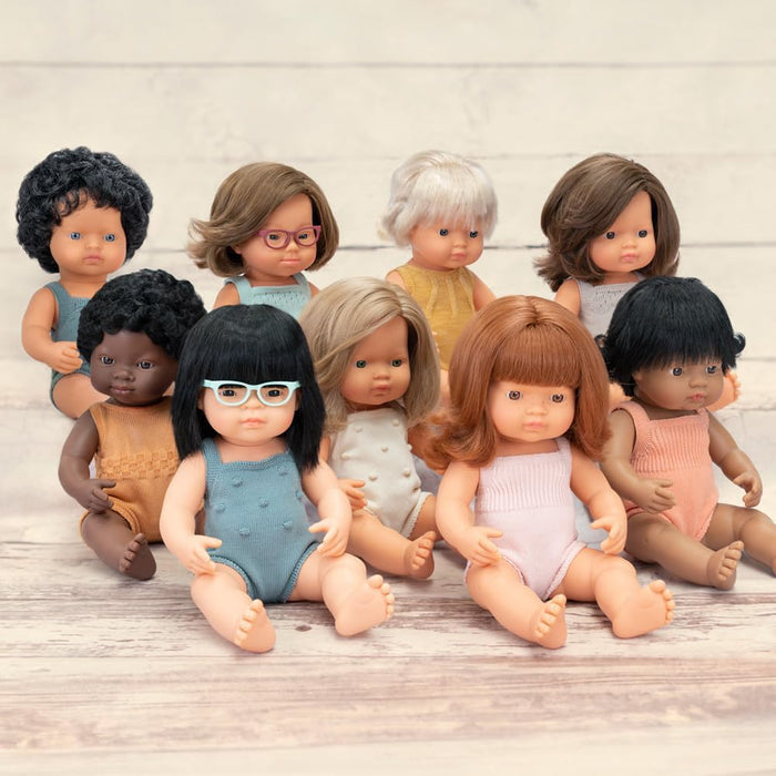 Nine diverse baby dolls with various skin tones and hair styles sitting together in colorful knit rompers.
