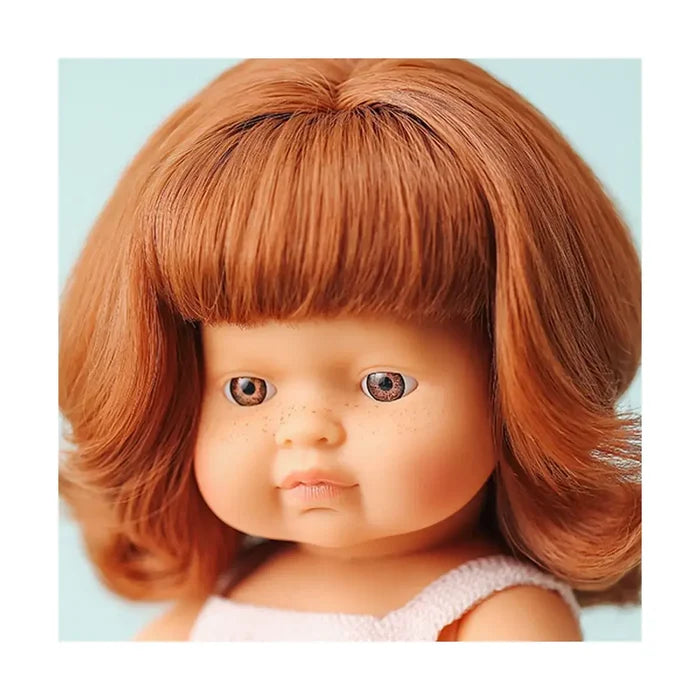 Close-up of a doll with thick red hair and bangs, brown eyes, and light freckles on her round, chubby cheeks.