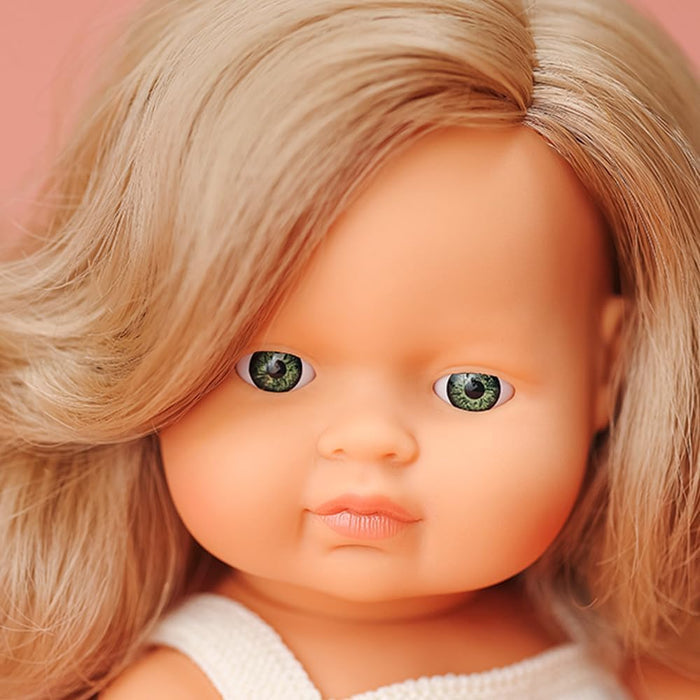 Close-up of a doll with wavy dark blonde hair, green eyes, and a white knit top against a soft pink background.