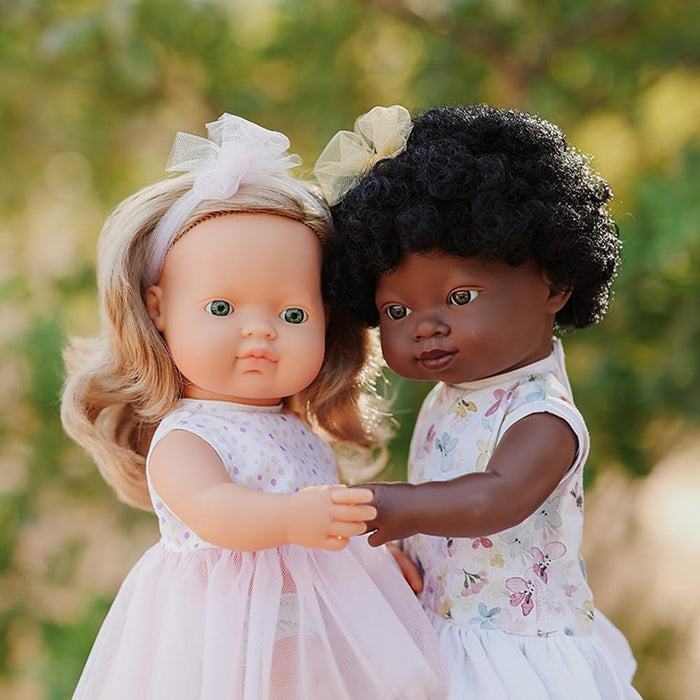 Dark blonde doll with green eyes, wavy hair, and a pink tulle dress holding hands with another doll outdoors.