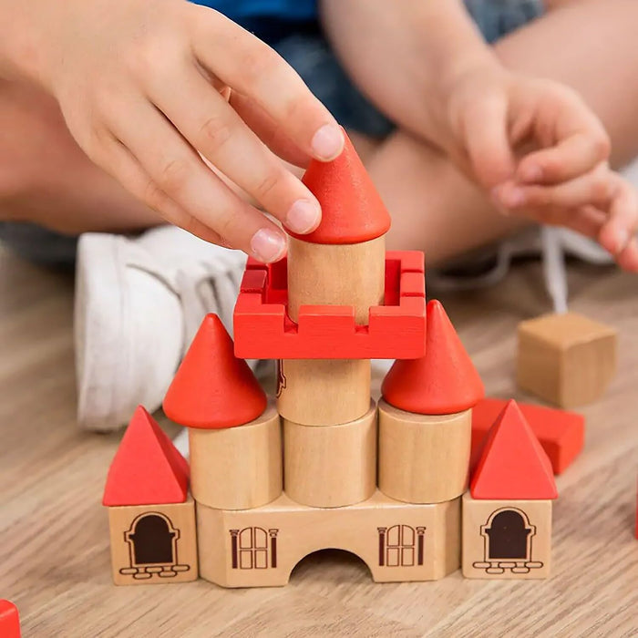 Child builds a wooden toy castle with red and natural blocks featuring cone-shaped roofs and tower cylinders.