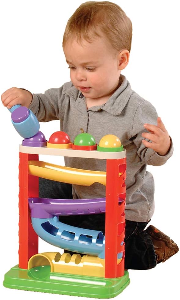 Toddler using a toy mallet to hit colorful balls down a multi-colored plastic ball run tower with three winding ramps.