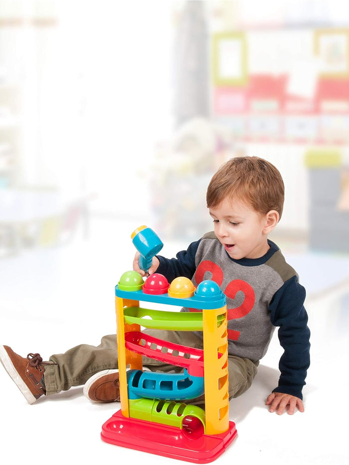 Toddler hitting colored balls through a four-level bright plastic ramp tower with a blue toy hammer.