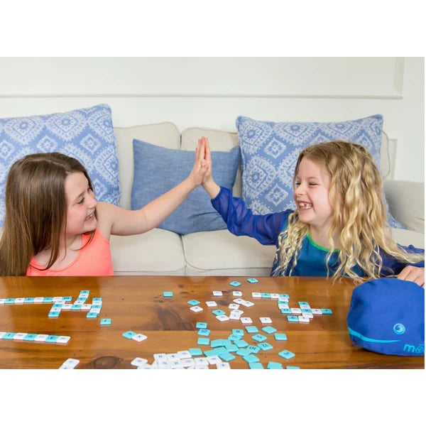 Two smiling girls high-five while playing with blue and white number tiles next to a blue whale-shaped pouch.