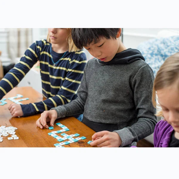 Three children playing with small blue and white square number and math symbol tiles on a wooden table.
