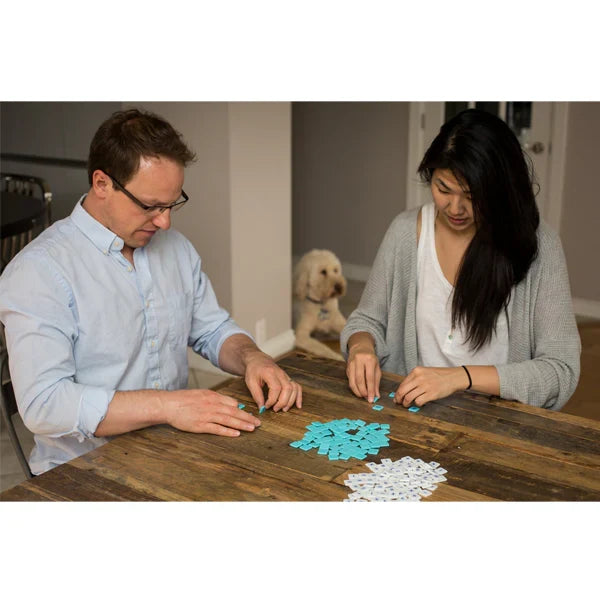 Two people playing with small light blue and white square number tiles on a rustic wooden table.