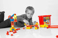 Child builds a crane and car using red, yellow, and blue plastic pieces next to a red storage tub on a white floor.