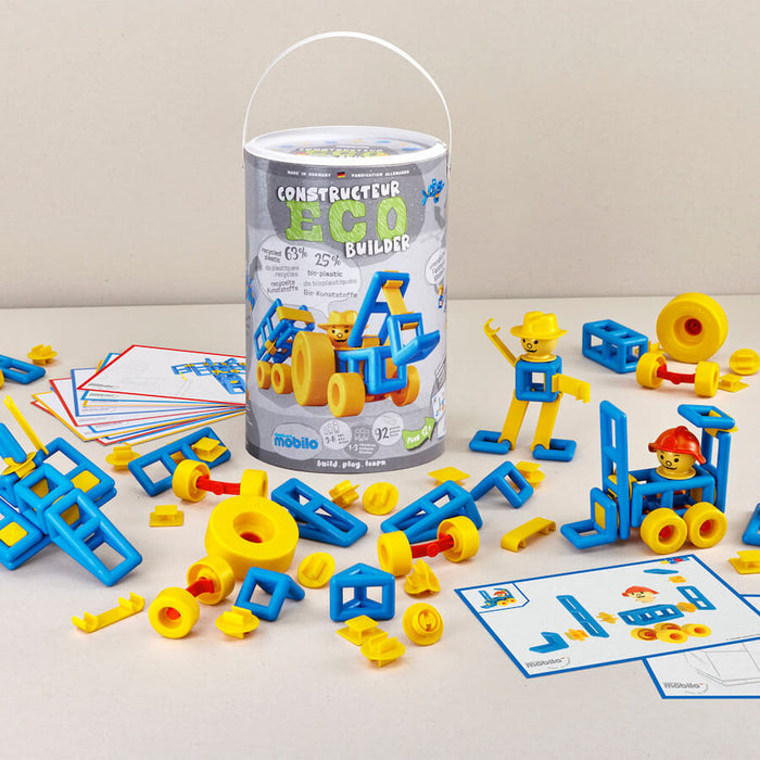 Blue and yellow plastic building pieces, figures, and models scattered around a white cylindrical storage container.