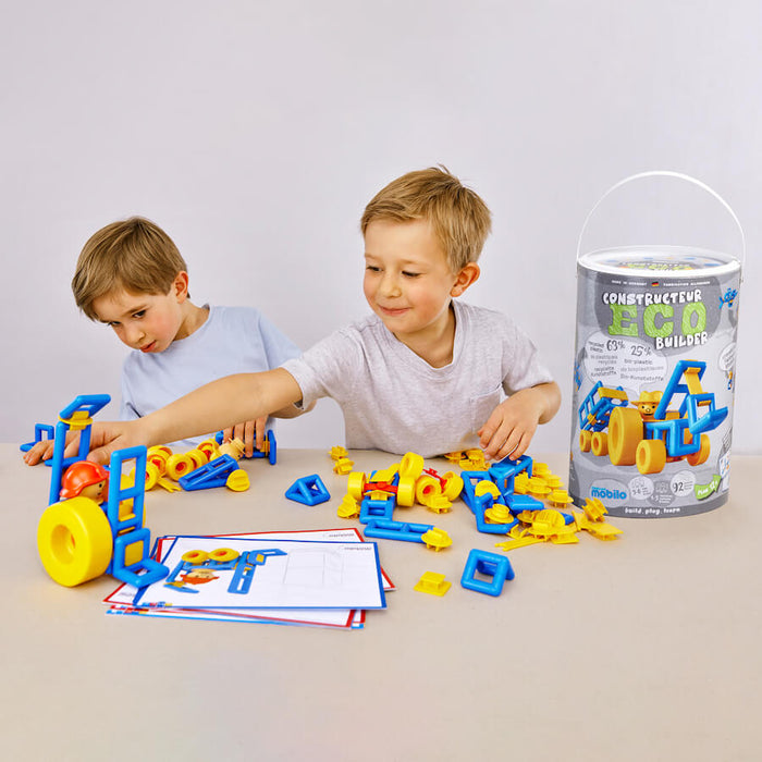 Two young boys build vehicles with yellow and blue plastic pieces from the Mobilo Eco Builder set on a white table.