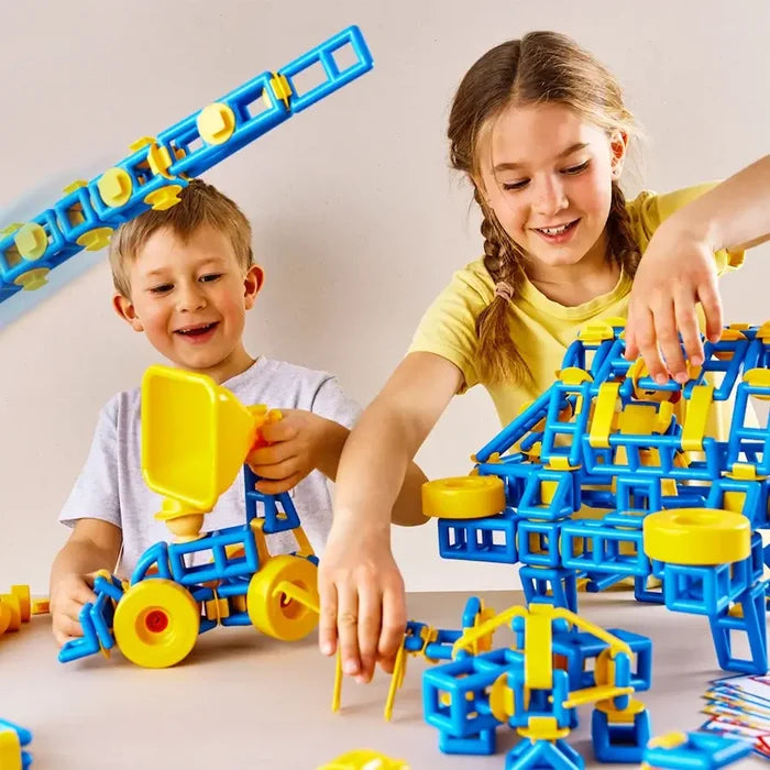 Two children building toy vehicles with blue and yellow square-framed plastic blocks and large yellow wheels.