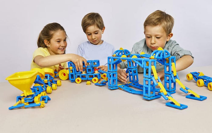 Three children building vehicles and a bridge using blue and yellow geometric plastic construction pieces.