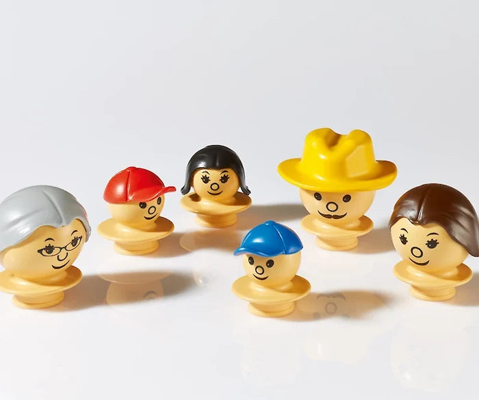 Six beige plastic toy figurines with various hairstyles and hats, like a yellow cowboy hat, on a white background.