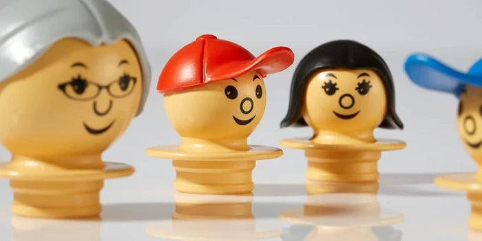 Four yellow toy figurines with different hair and hats, including a red cap and silver hair with glasses.